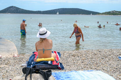Djevojka sa šeširom se sunča na plaži. Djevojka sa šeširom se sunča na plaži. Turisti na moru. Ljetni godišnji odmor.