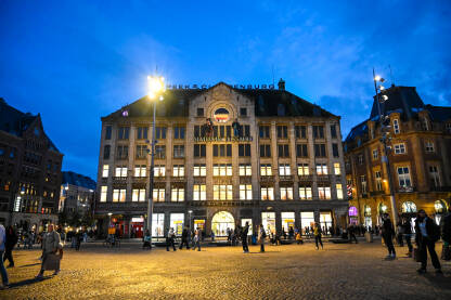 Kraljevska palača u Amsterdamu, Nizozemska. Ljudi na trgu Dam u centru grada noću. Historijska znamenitost u Amsterdamu.