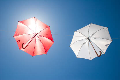 Crveni i bijeli kišobran, zakačeni na žicu iznad ulice. Umjetnička instalacija. Intervencija u prostoru.