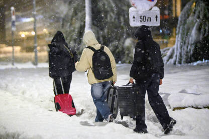 Ljudi s prtljagom hodaju kroz snijeg. Mladi ljudi s torbama i ruksacima hodaju kroz snježnu mećavu zimi.