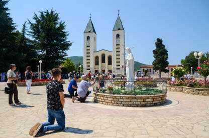 Katolički hodočasnici Katolički hodočasnici mole se u Međugorju, Bosna i Hercegovina. Ljudi prisustvuju svetoj misi. Crkva i kip Djevice Marije.