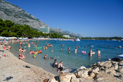 Plaža u Makarskoj puna ljudi Turisti na moru. Ljudi se kupaju i sunčaju u Jadranskom moru. Ljetni odmor. Grupa turista na plaži tokom toplog ljetnog dana. Makarska, Hrvatska.