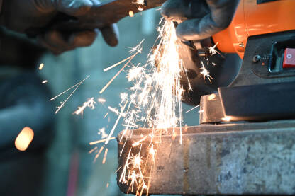 AKA_0196 (2) Radnik brusi metal na poslu. Iskre iz brusilice. Obrada čelika. Iskre lete iz električne brusilice, krupni plan. Industrijski radnik na gradilištu.