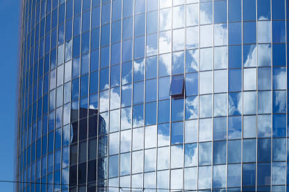 Fotografija moderne staklene poslovne zgrade sa jednim otvorenim prozorom i refleksijom oblaka.Urbana arhitektura.