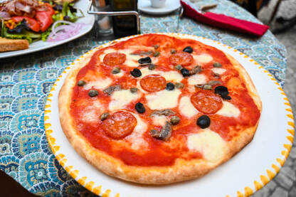 Pizza na stolu u restoranu Pizza na stolu u restoranu. Pizza s sudžukom, povrćem, maslinama i sirom.