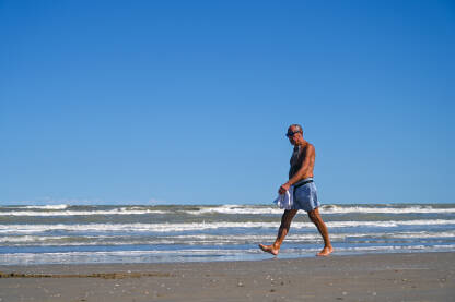 Stariji muškarac uživa u šetnji uz more Čovjek šeta pješčanom plažom u blizini mora. Stariji muškarac uživa u šetnji uz more.