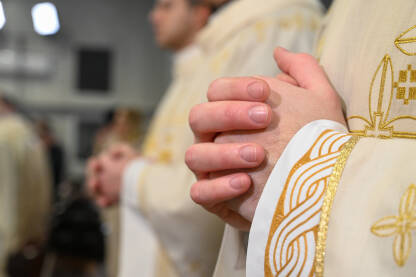 Katolički svećenici u liturgijskim odorama se mole Katolički svećenici u liturgijskim odorama se mole sa sklopljenim rukama. Ruke čovjeka koji se moli u katedrali. Božićna misa polnoćka u crkvi.