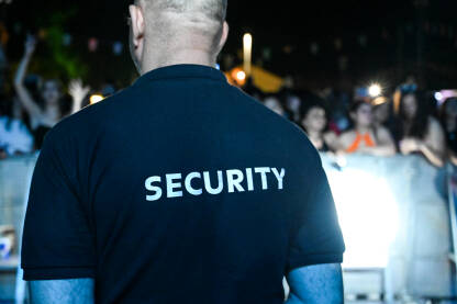 Obezbjeđenje na koncertu Zaštitar nosi majicu sa natpisom security. Zaštitar stoji ispred publike tokom muzičkog festivala.