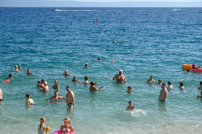Ljudi se kupaju u moru Turisti na moru. Ljudi se kupaju i sunčaju u Jadranskom moru. Ljetni odmor. Grupa turista na plaži tokom toplog ljetnog dana. Makarska, Hrvatska.