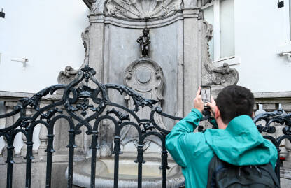 Bruxelles, Belgija. Turist fotografira skulpturu u gradu. Bruxelles, Belgija. Turist fotografira Maneken Pis, simbol Brisela. Poznata znamenitost, skulptura od bronzane fontane u centru grada.