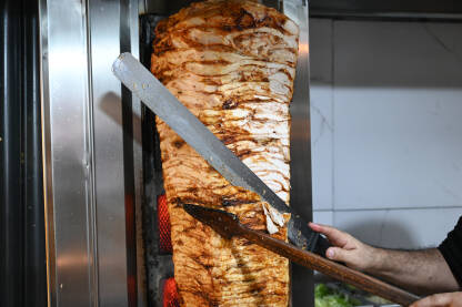 Ukusni donner kebab. Pečeno donner meso na rotiranom ražnju. Kuhar reže meso. Ukusni donner kebab.