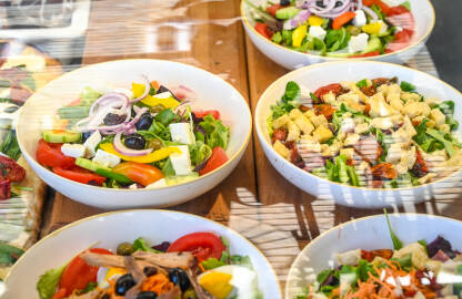 Svježa salata u zdjelama u restoranu. Nasjeckano povrće u zdjeli. Paradajz, luk, sir, rukola, masline.