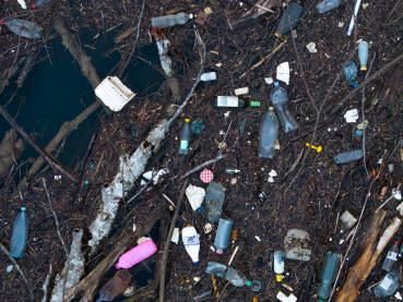 Razni oblici komunalnog otpada nagomilani u rijeci Drini, vidljivi na površini i uz obalu.