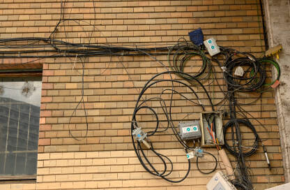 Žice od telefona, interneta, kablovske televizije i drugih servisa umotani u veliko klupko na fasadi zgrade. Kablovi na ulazu u zgradu.